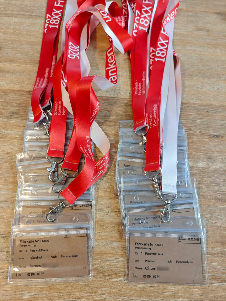 Mehrere Lanyards mit Contickets im Stil alter Bahntickets liegen auf einem Holztisch.
